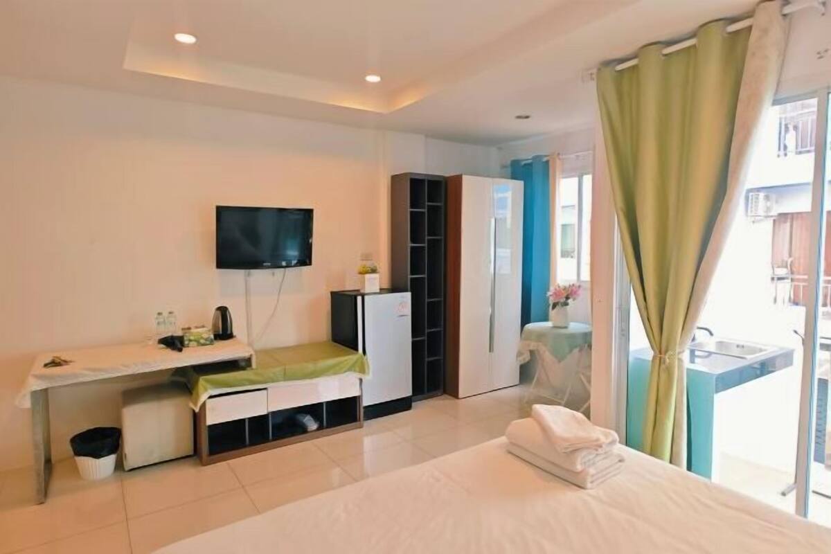 A hotel room with a bed, a desk with a television, a wardrobe, and a balcony with a sink.