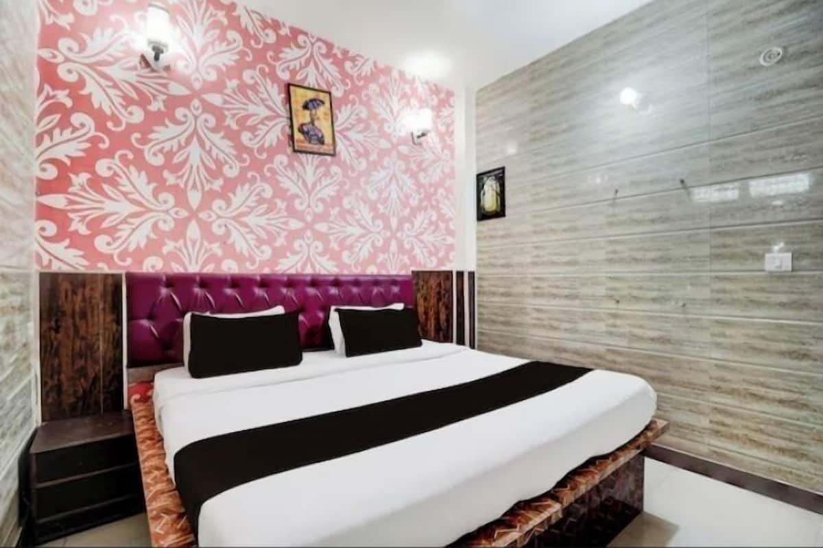 Un dormitorio moderno con cabecera capitonada, una cama grande con ropa de cama blanco y negro, una pared con estampado rosa y una pared revestida de baldosas grises.