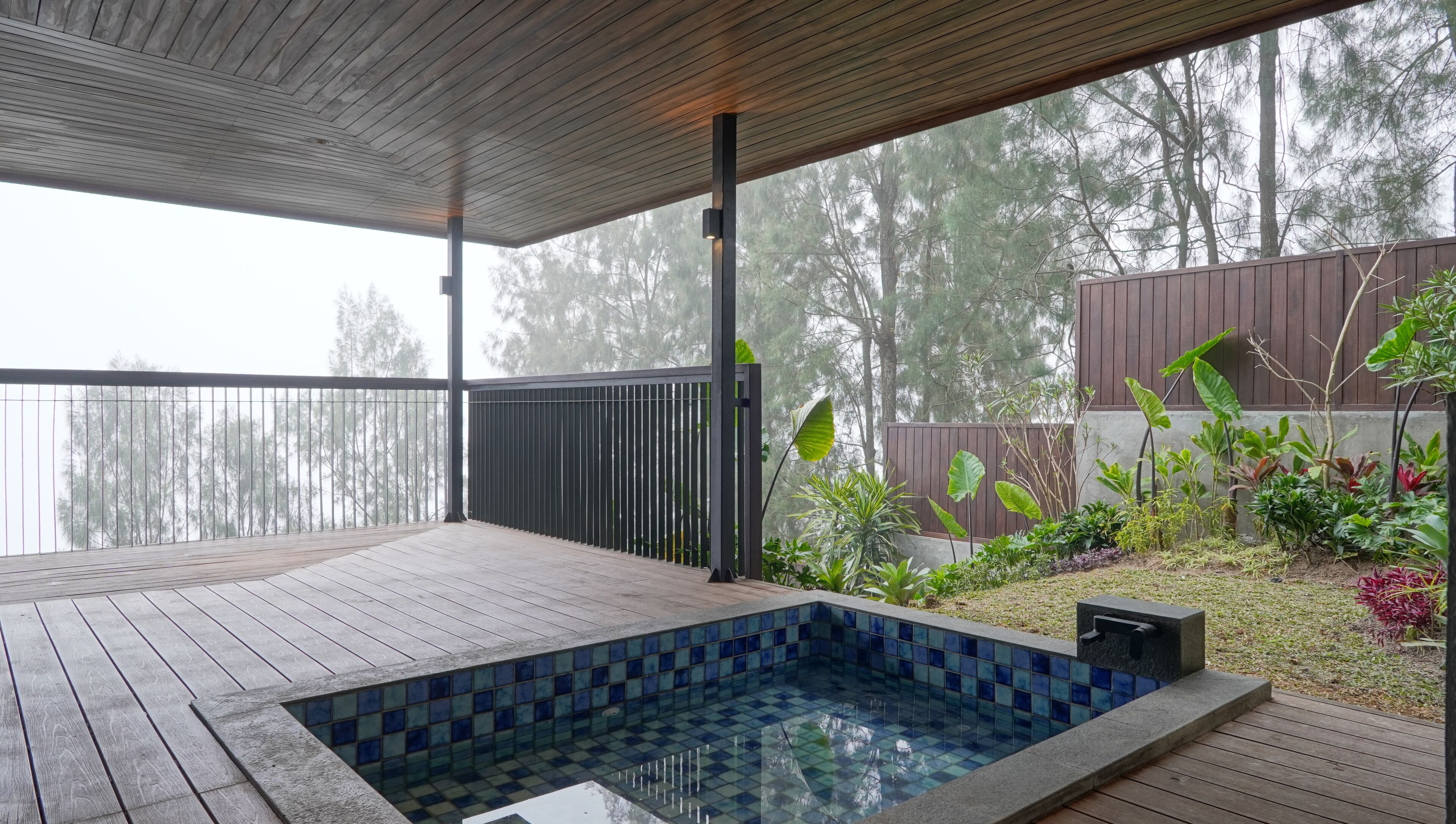 A wooden deck with a swimming pool, surrounded by plants and a view of trees.