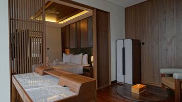 A hotel room with a bed, a desk, a chair, a bedside table, and a refrigerator.