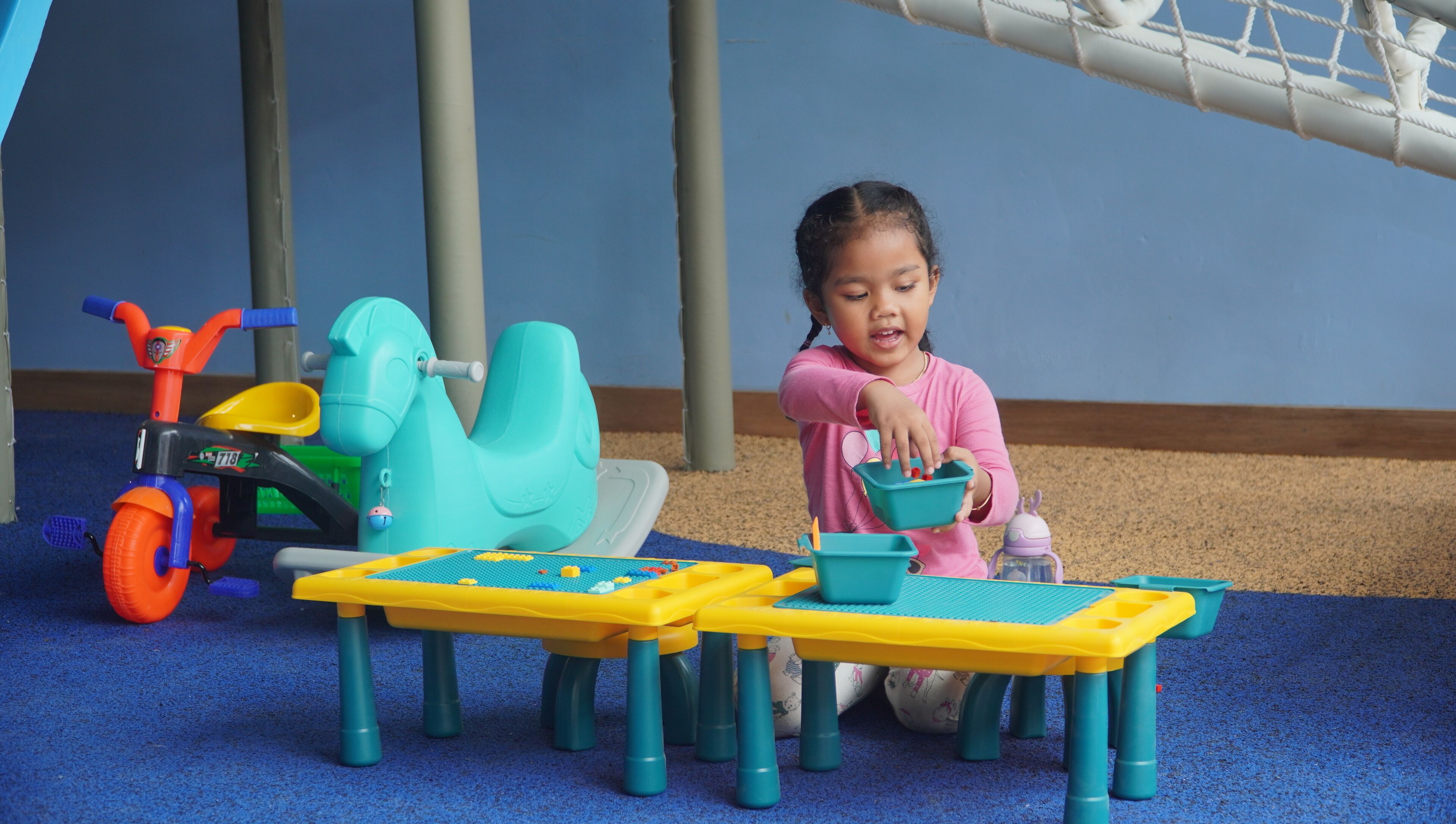 Uma criança brincando com brinquedos em um chão coberto por carpete azul.