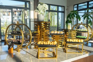 Una mesa de buffet con múltiples puestos de servicio con marcos dorados, diversas opciones de productos horneados y una planta en maceta.