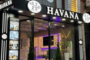 The exterior of the Havana Hotel & Suites with a modern facade, illuminated signage, and a view of the interior through the glass doors. - Havana Hotel Suites (Istanbul)