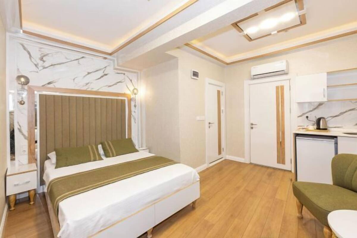 A bedroom with a bed, bedside table, lamp, and a small kitchenette area with a microwave and kettle.