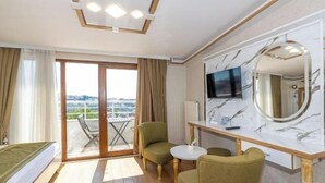 A hotel room with a bed, a desk with a TV, a chair, a small table, and a balcony with a view. - Havana Hotel Suites (Istanbul)