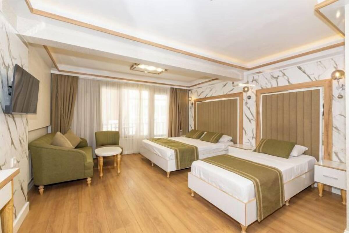 A hotel room with two beds, a sofa, a small round table, and a TV mounted on the wall.