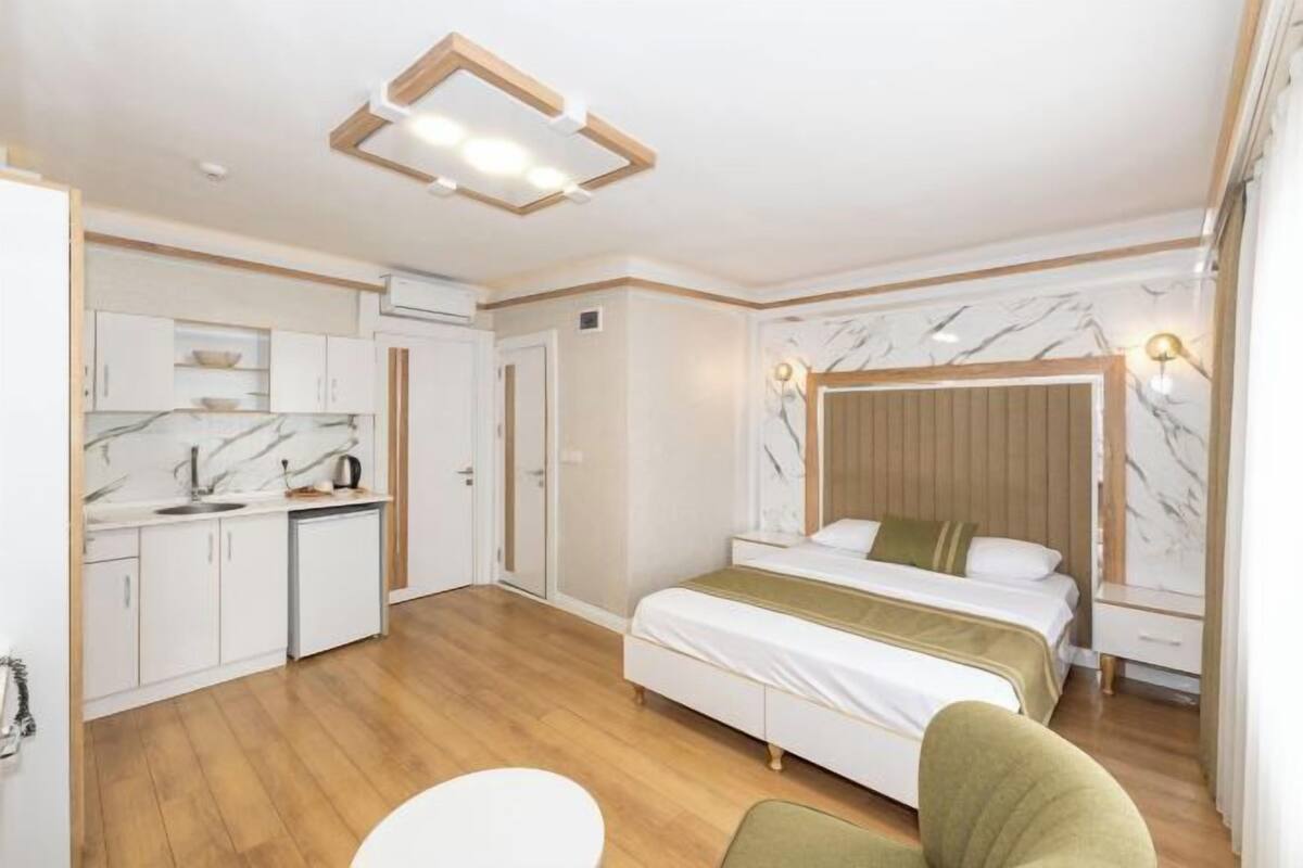 A compact hotel room with a bed, bedside table, and a small kitchenette.