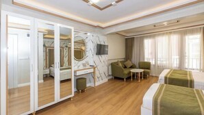 A hotel room with a wooden floor, a desk with a chair, a sofa, two beds, a TV, and a mirror. - Havana Hotel Suites (Istanbul)