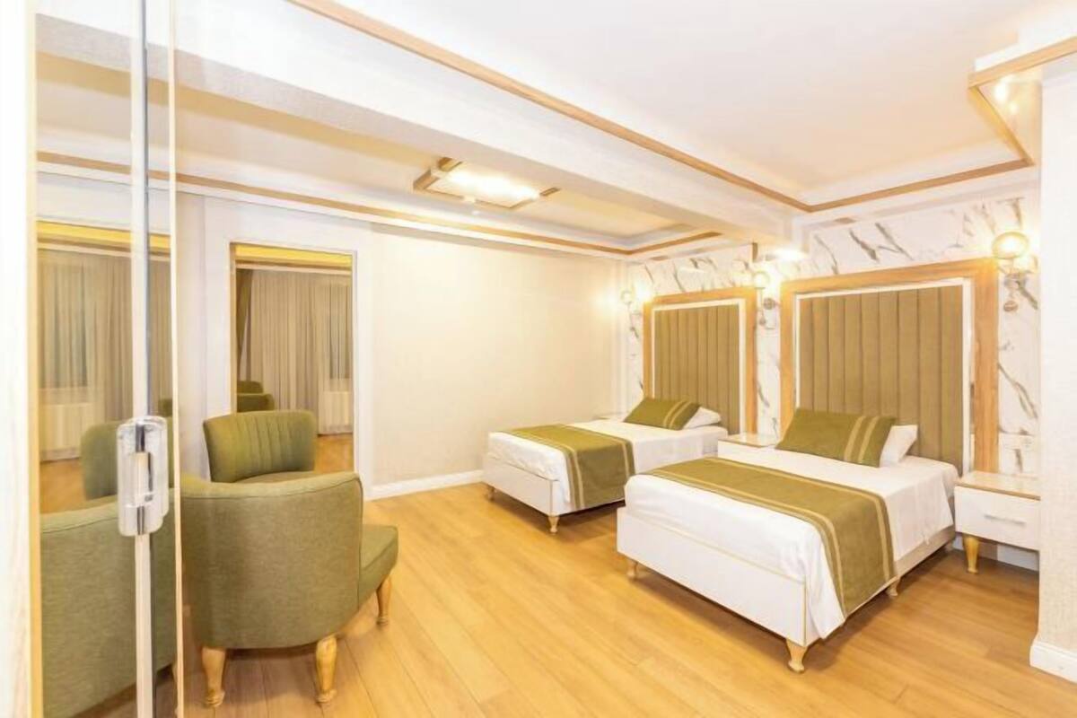A hotel room with two beds, a green armchair, and a wooden floor.