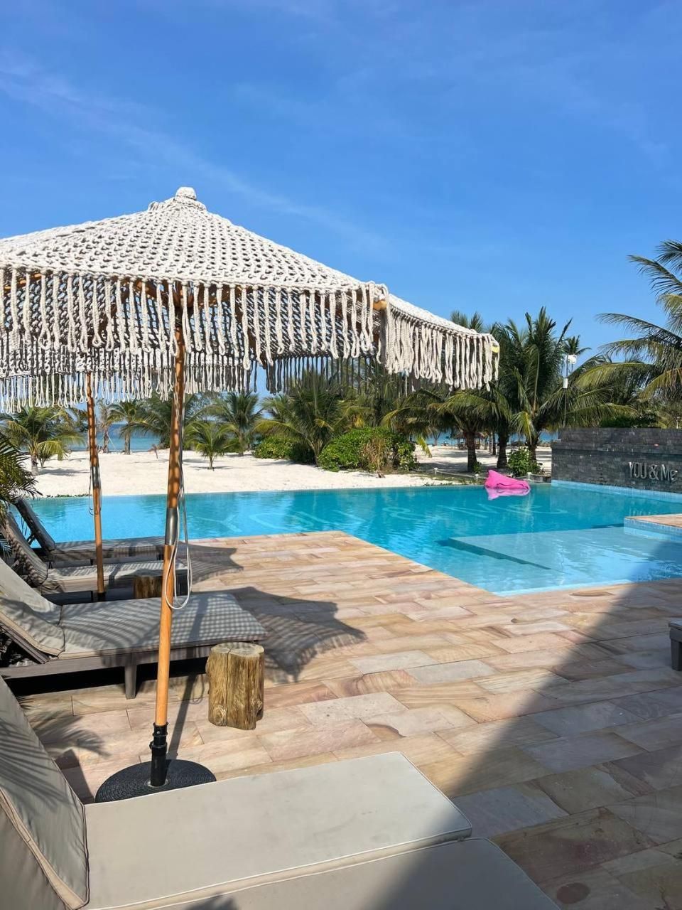 Uma área de piscina com um bangalô, espreguiçadeiras e vista clara para a praia.