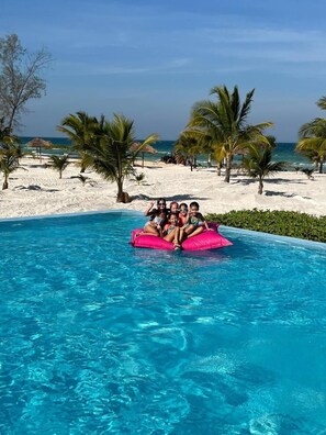 Una piscina con acqua cristallina, circondata da palme e da una spiaggia sabbiosa.