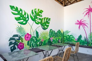 A dining area with a mural of tropical plants, tables, and chairs. - You Me Resort (Koh Rong)