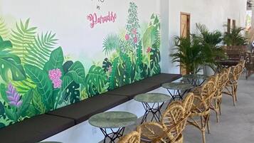 Een restaurant met een muurschildering, rieten stoelen en tafels.