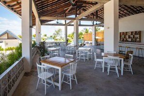 An outdoor patio area with white tables and chairs, a wooden ceiling, and a view of the beach. - You Me Resort (Koh Rong)