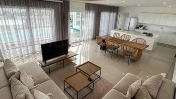 Ein modernes Wohnzimmer mit einer Couch, einem Couchtisch, einem Fernseher und einem Essbereich mit Stühlen und einem Tisch.