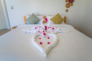 Una camera d'albergo con un letto rifatto, un'accattivante composizione di asciugamani a forma di cuore e cuscini decorativi.
