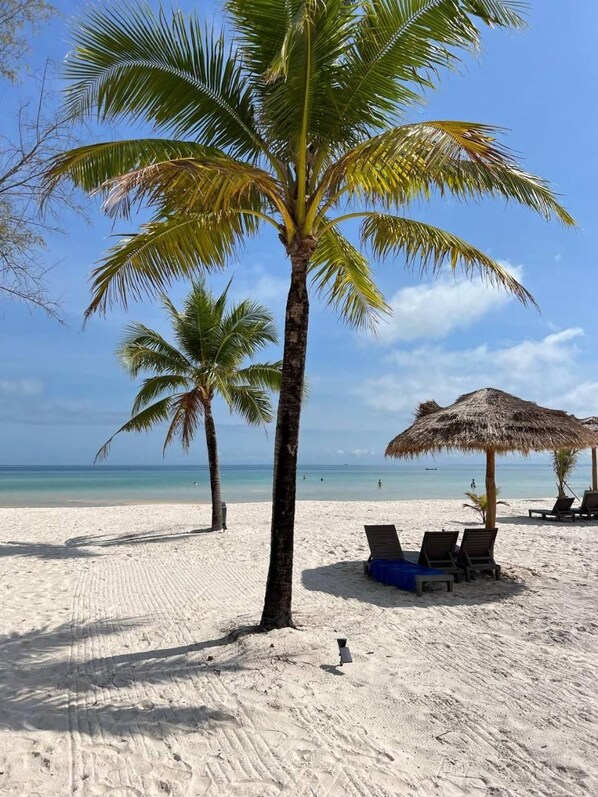 A beach with palm trees, a thatched umbrella, and lounge chairs. - You Me Resort (Koh Rong)