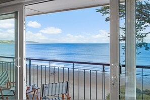 A balcony with a view of the sea, a chair, a table, and a railing. - 33 Beach Court - Direct Beach Access Sea Views (Saundersfoot)