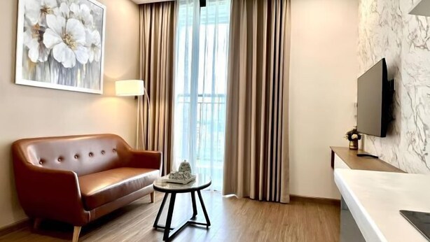Ein modernes Hotelzimmer mit einer Ledersofa, einem kleinen runden Tisch, einem flachbildfernseher an der Wand und einem großen Fenster mit Vorhängen.