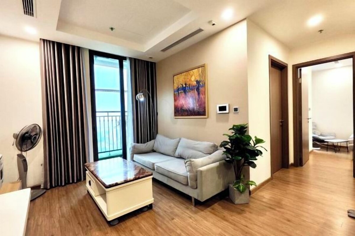 A modern living room with a sofa, a small table, a potted plant, a painting on the wall, and a sliding door leading to another room.