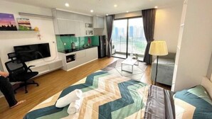 A modern hotel room with a large bed, a TV, a kitchenette, and a balcony with a view of the city. - HKG - Vinhome GreenBay - Green apartment in Hanoi (Hanoi)
