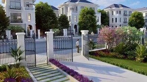 A gated residential area with multiple white houses, a well-maintained lawn, and a gated entrance. - HKG - Vinhome GreenBay - Green apartment in Hanoi (Hanoi)