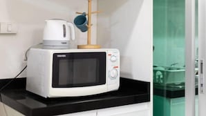 A microwave oven on a black countertop with a Toshiba logo, a wooden rack with a blue mug, and a glass enclosure in the background. - Bella Rama 9 Apartment Bangkok [near central rama 9 shopping mall + Phra Rama 9 subway station] (Bangkok)