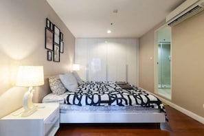 Een slaapkamer met een bed, nachtkastje, lamp en een kledingkast.