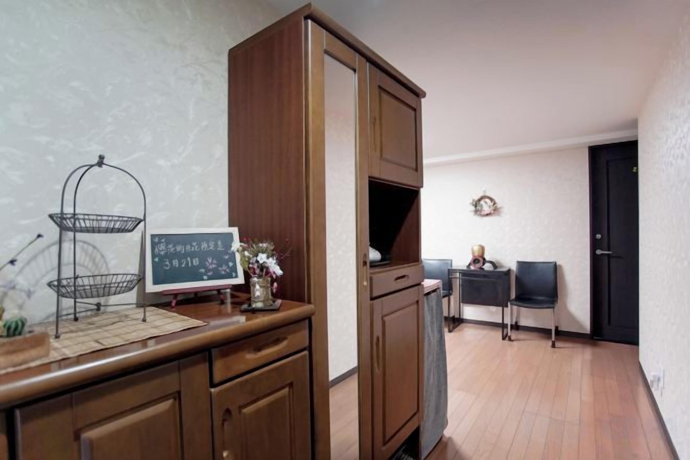 A room with a wooden cabinet, a small table with a basket, a framed picture, and a door in the background.