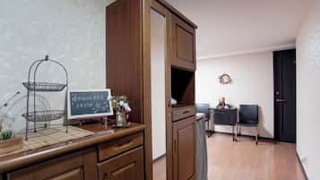 A room with a wooden cabinet, a small table with a basket, a framed picture, and a door in the background.