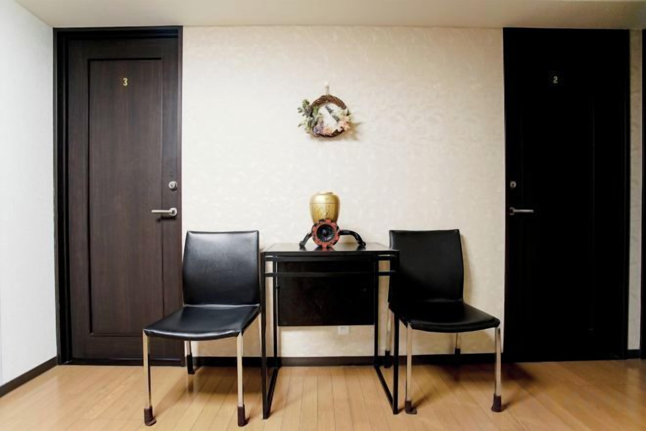 A room with two black chairs, a small table with a decorative item, and two doors.