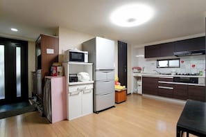 A modern kitchen with a refrigerator, microwave, and stove, wooden flooring, and a dining area with a table. - Tokyo Wenjuan's Guesthouse (Tokyo)