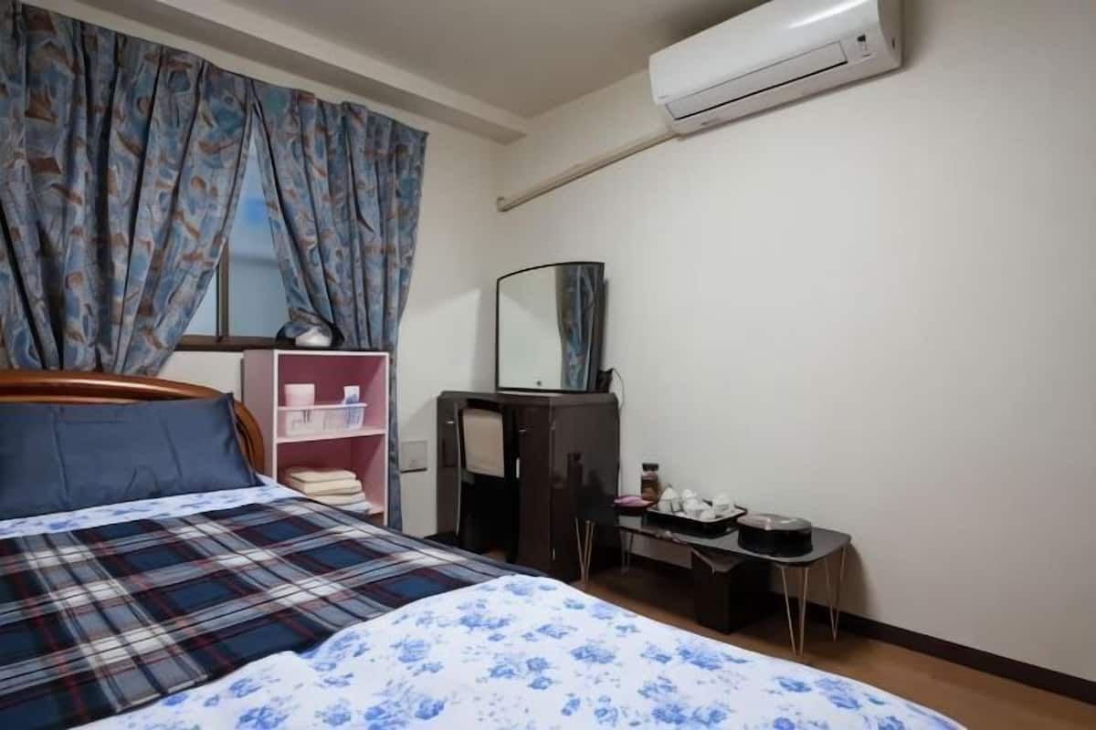 Une chambre à coucher avec un lit, une commode, un miroir, une petite table et une fenêtre avec des rideaux.