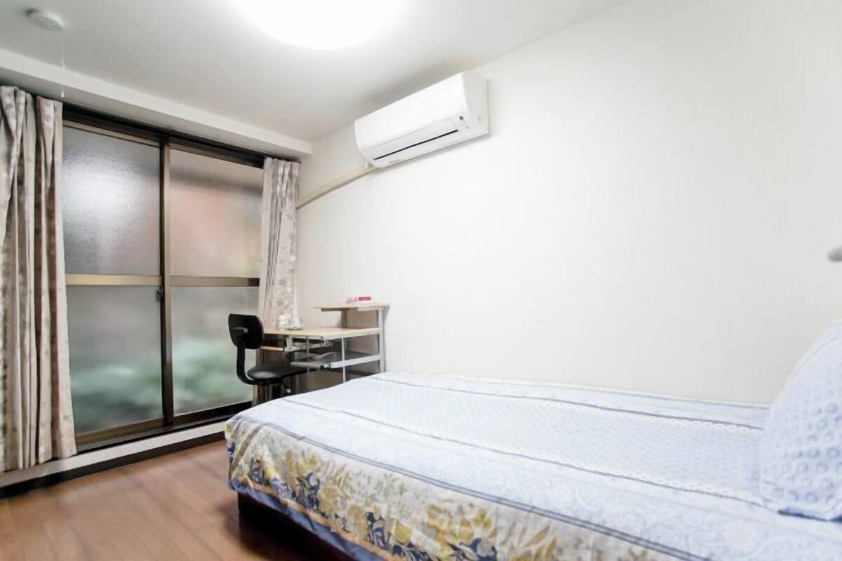 Une chambre d’hôtel équipée d’un lit, d’un bureau, d’une chaise, d’un climatiseur et d’une porte-fenêtre coulissante.