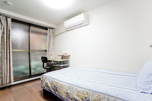 Une chambre d’hôtel équipée d’un lit, d’un bureau, d’une chaise, d’un climatiseur et d’une porte-fenêtre coulissante.