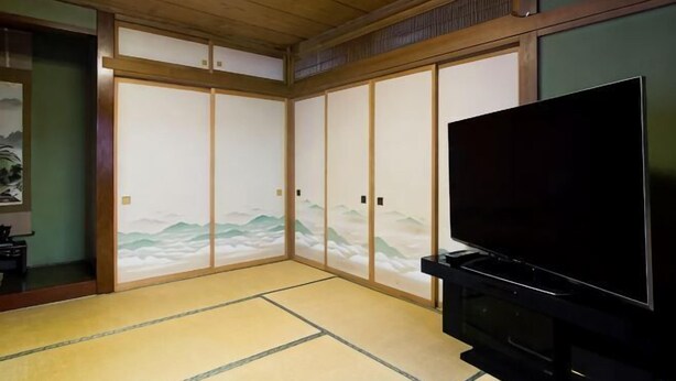 Una tradizionale stanza giapponese con pavimento in tatami, porte scorrevoli, una televisione e un tavolino in legno.