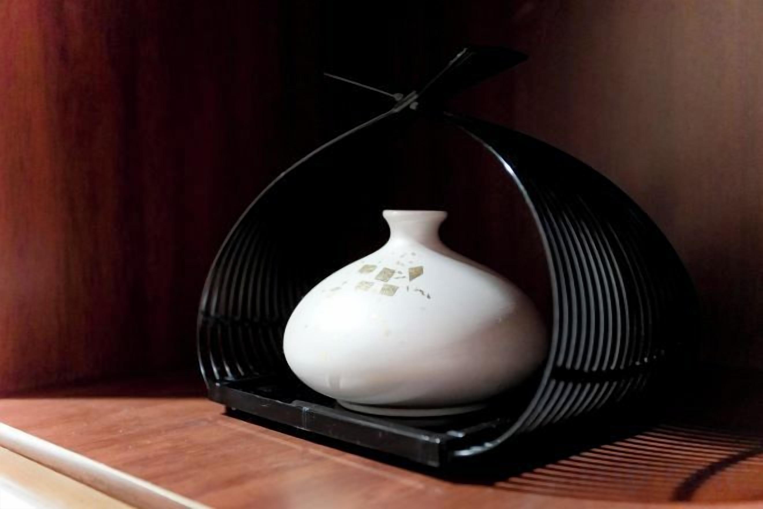 A white ceramic vase on a black stand in a wooden room.