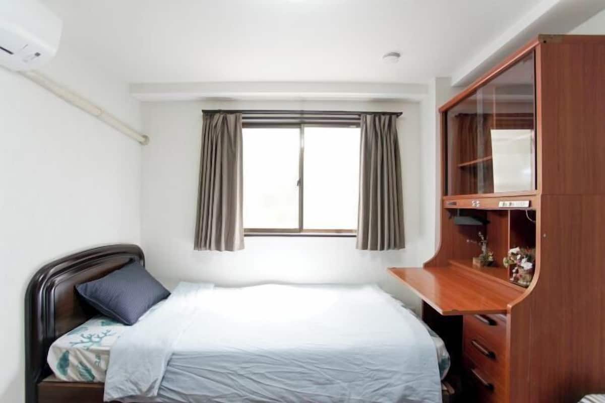 Une chambre à coucher comprenant un lit, une armoire en bois, une fenêtre avec des rideaux et un climatiseur fixé au mur.