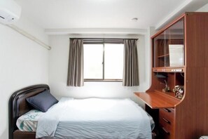 Une chambre à coucher comprenant un lit, une armoire en bois, une fenêtre avec des rideaux et un climatiseur fixé au mur.