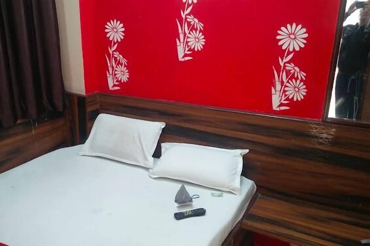 A hotel room with a wooden headboard, a white bedspread, two white pillows, and a remote control on the bed.
