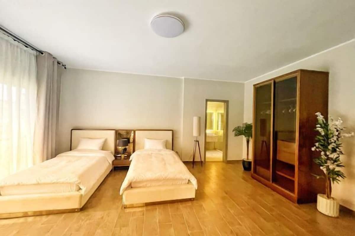 Une chambre d’hôtel avec deux lits, une armoire, une table de chevet, une lampe et une plante en pot.