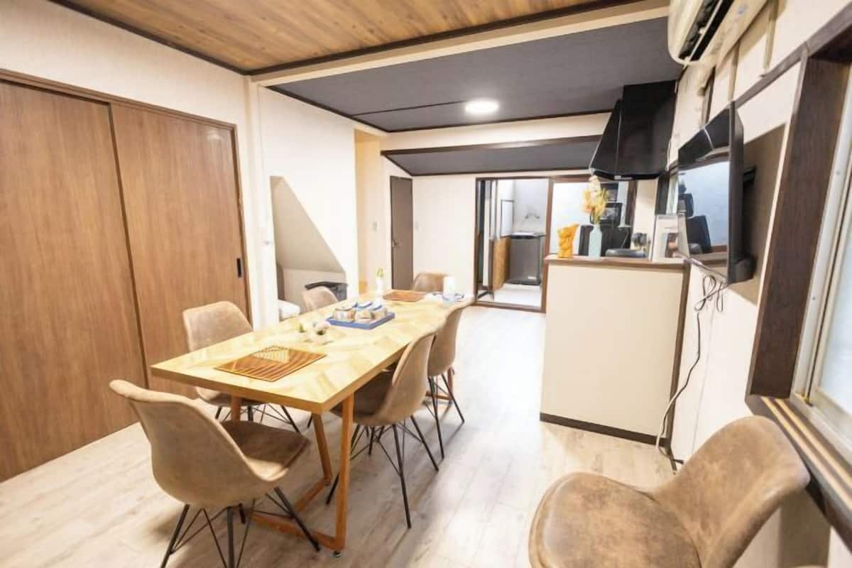 Een eethoek met een houten tafel en stoelen, een keuken met een koelkast, en een schuifdeurkast.