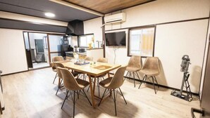 Un comedor con mesa y sillas de madera, una cocina al fondo y un televisor en la pared.
