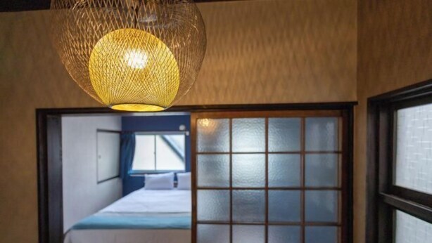 Una habitación con una cama, un ventanal con vidrio esmerilado y una lámpara colgante.