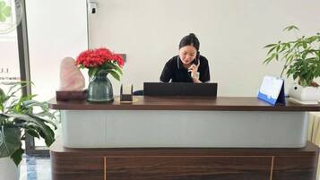 A reception desk with a laptop, a vase with red flowers, and a potted plant.