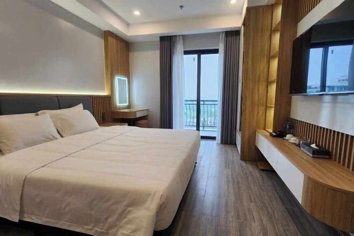 Een moderne hotelkamer met een groot bed, nachtkastje, televisie en balkon met gordijnen.