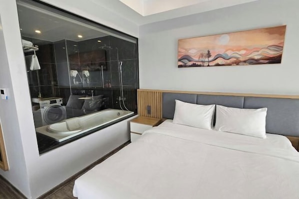 Una habitación de hotel moderna con una cama grande, una bañera, un tocador con espejo y un cuadro en la pared.