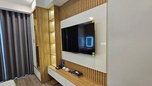 Une chambre d’hôtel moderne avec un téléviseur fixé au mur, un meuble console intégré et une grande fenêtre avec des rideaux.
