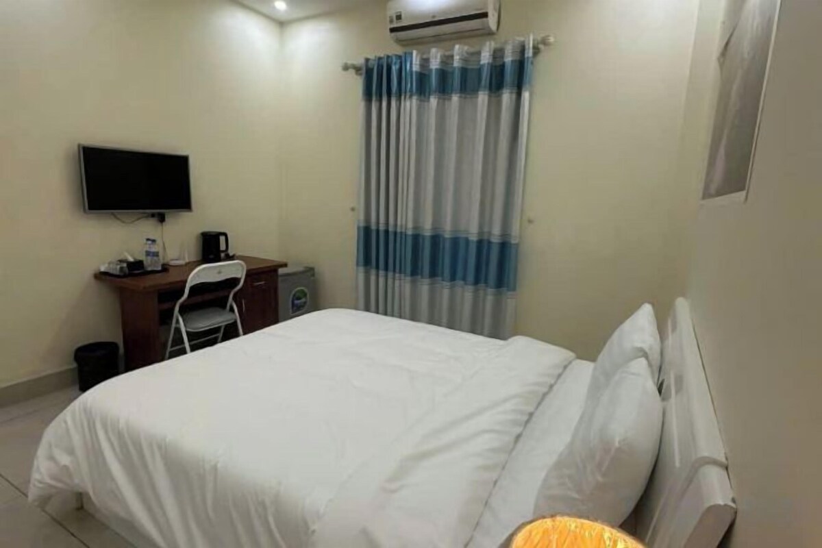 A hotel room with a bed, a desk with a chair, a television, and a window with curtains.