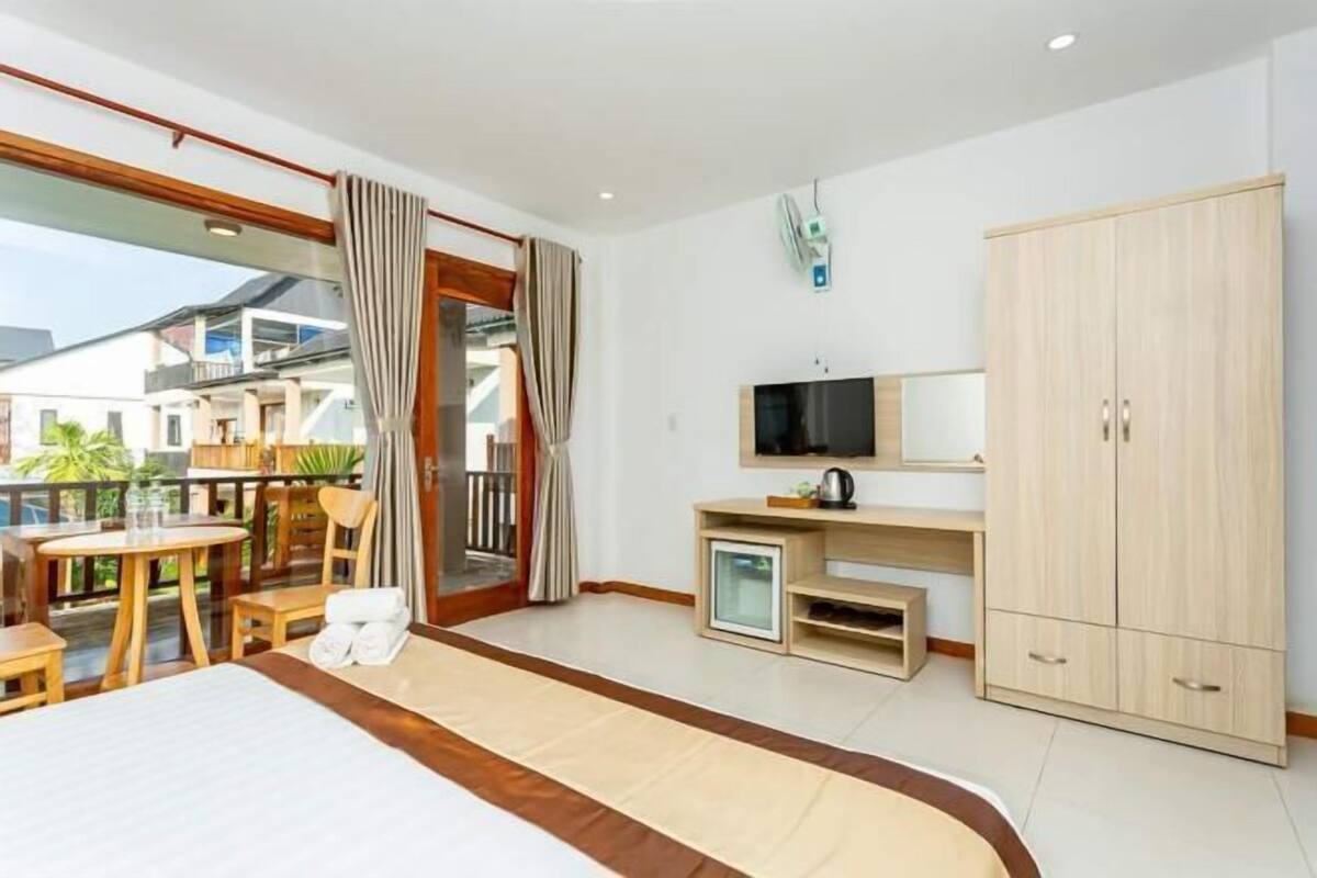 Une chambre d’hôtel comprenant un lit, une télévision, une armoire, une petite table avec des chaises et un balcon avec vue.